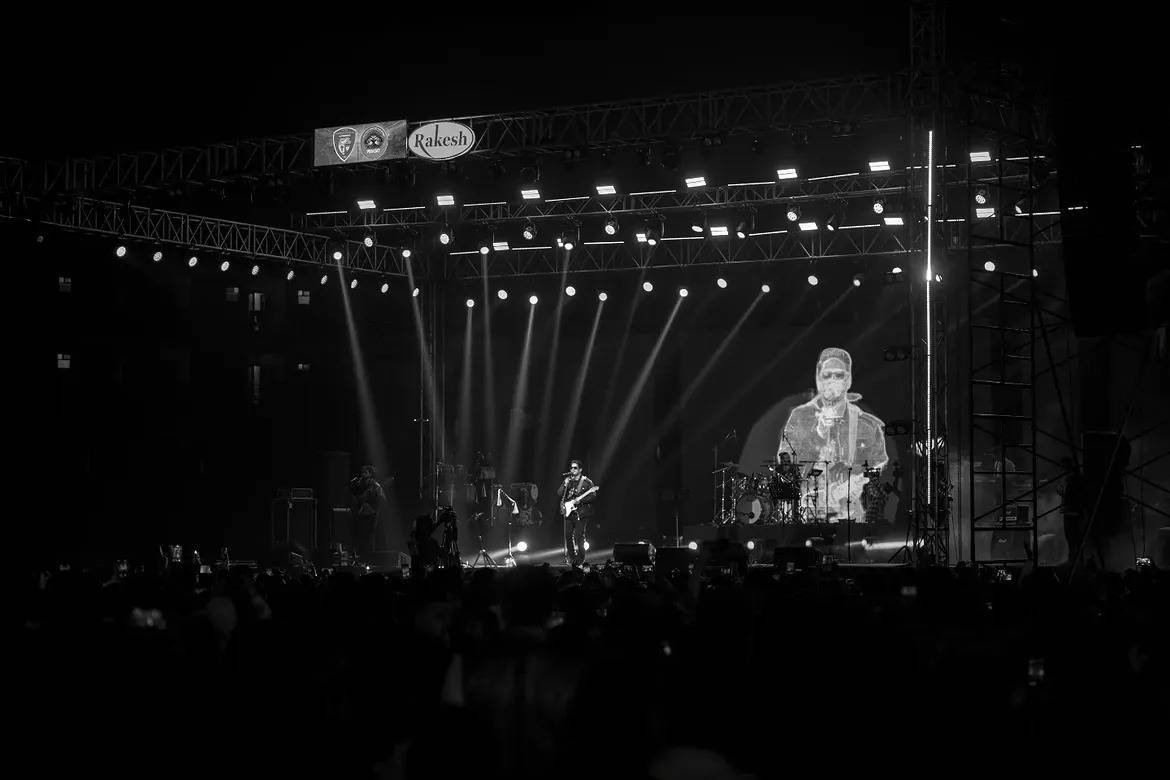 Black-and-white wide view of the Amit Mishra Live stage: lighting truss, beams and the artist on the LED screen.