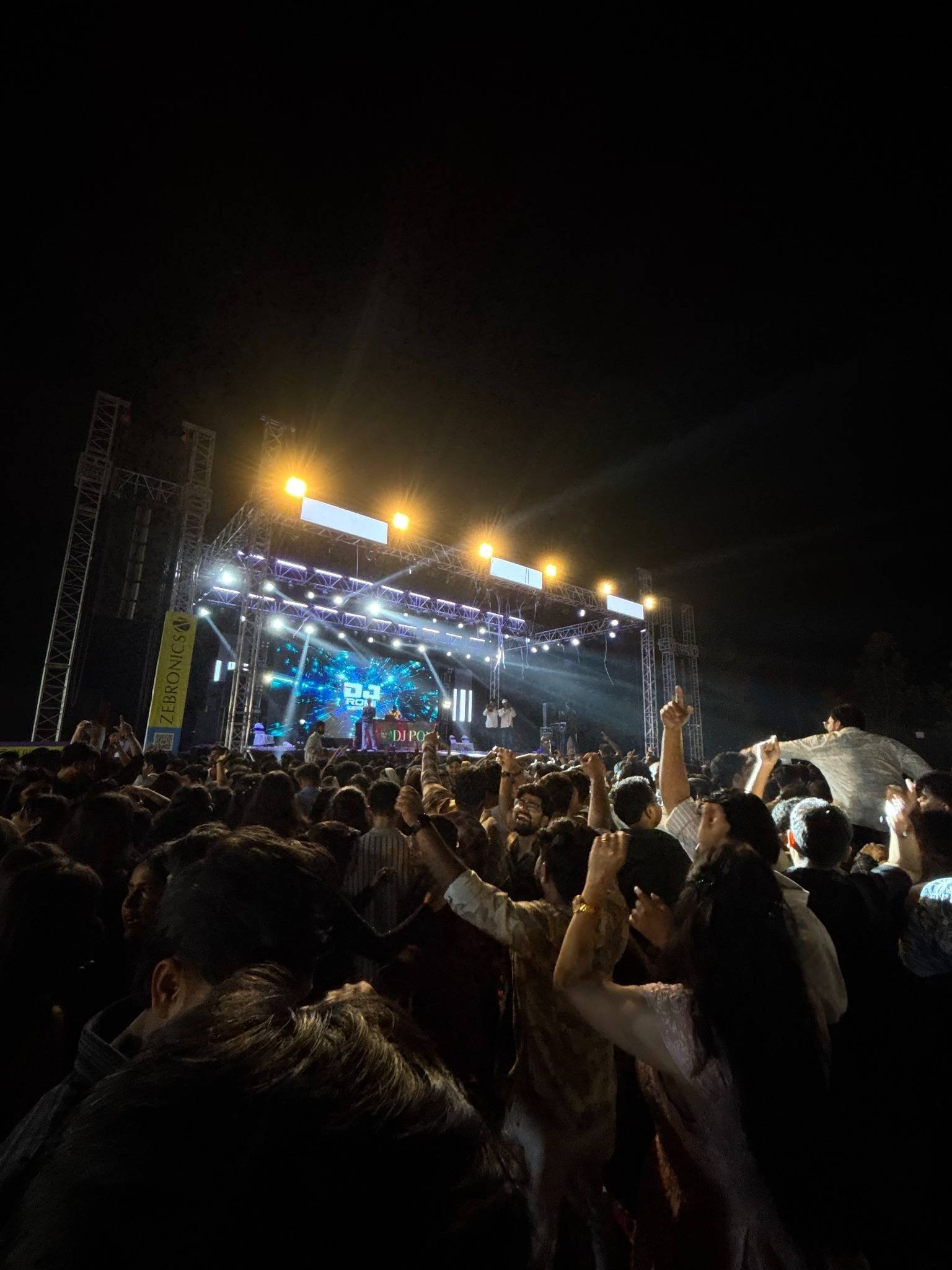 A crowd with raised hands in front of an illuminated concert stage.