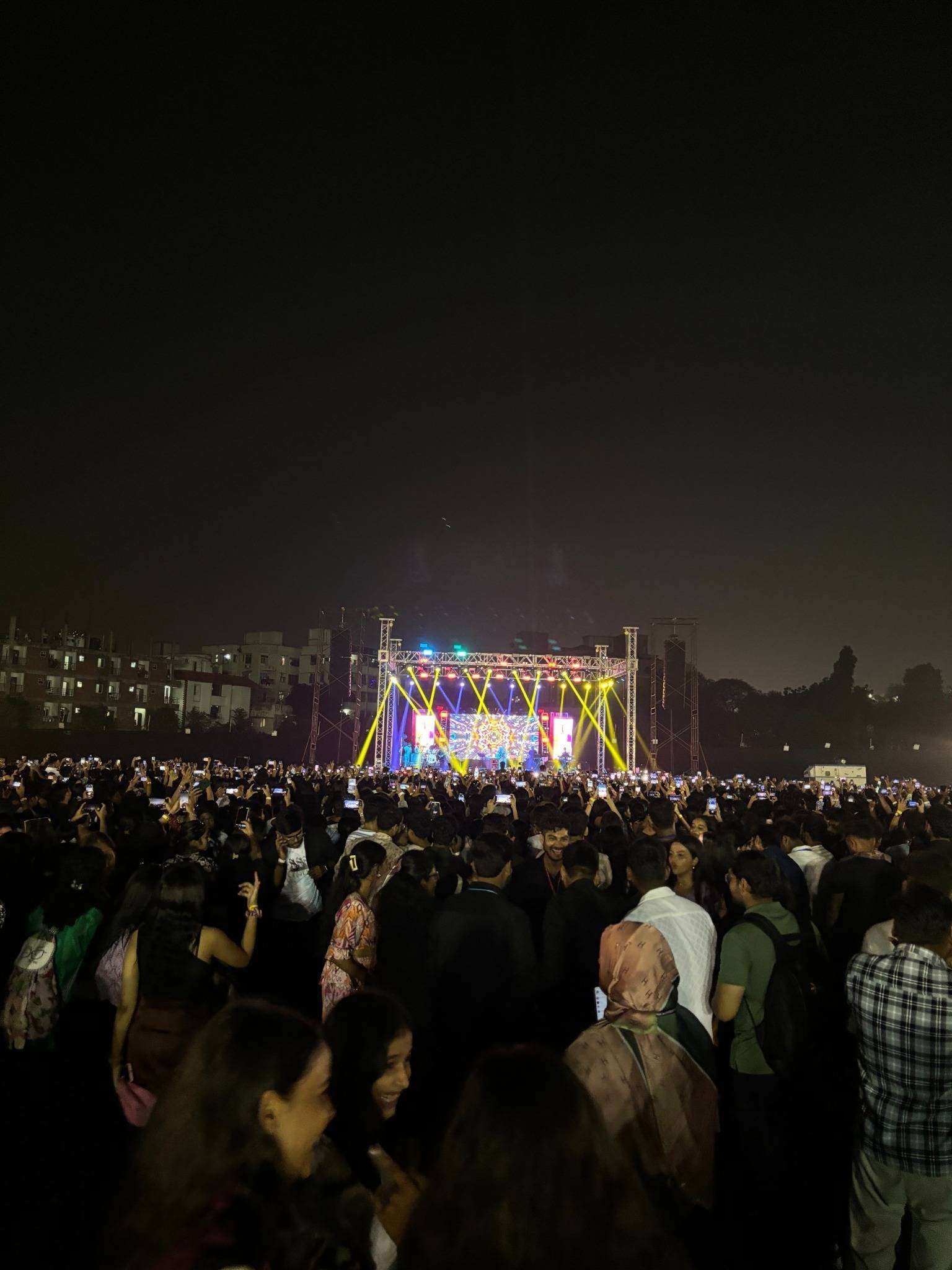 A vast night crowd facing a brightly lit concert stage in the distance.