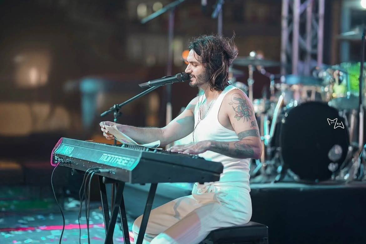 Gajendra Verma at the keyboard on stage, with drums and truss behind him.