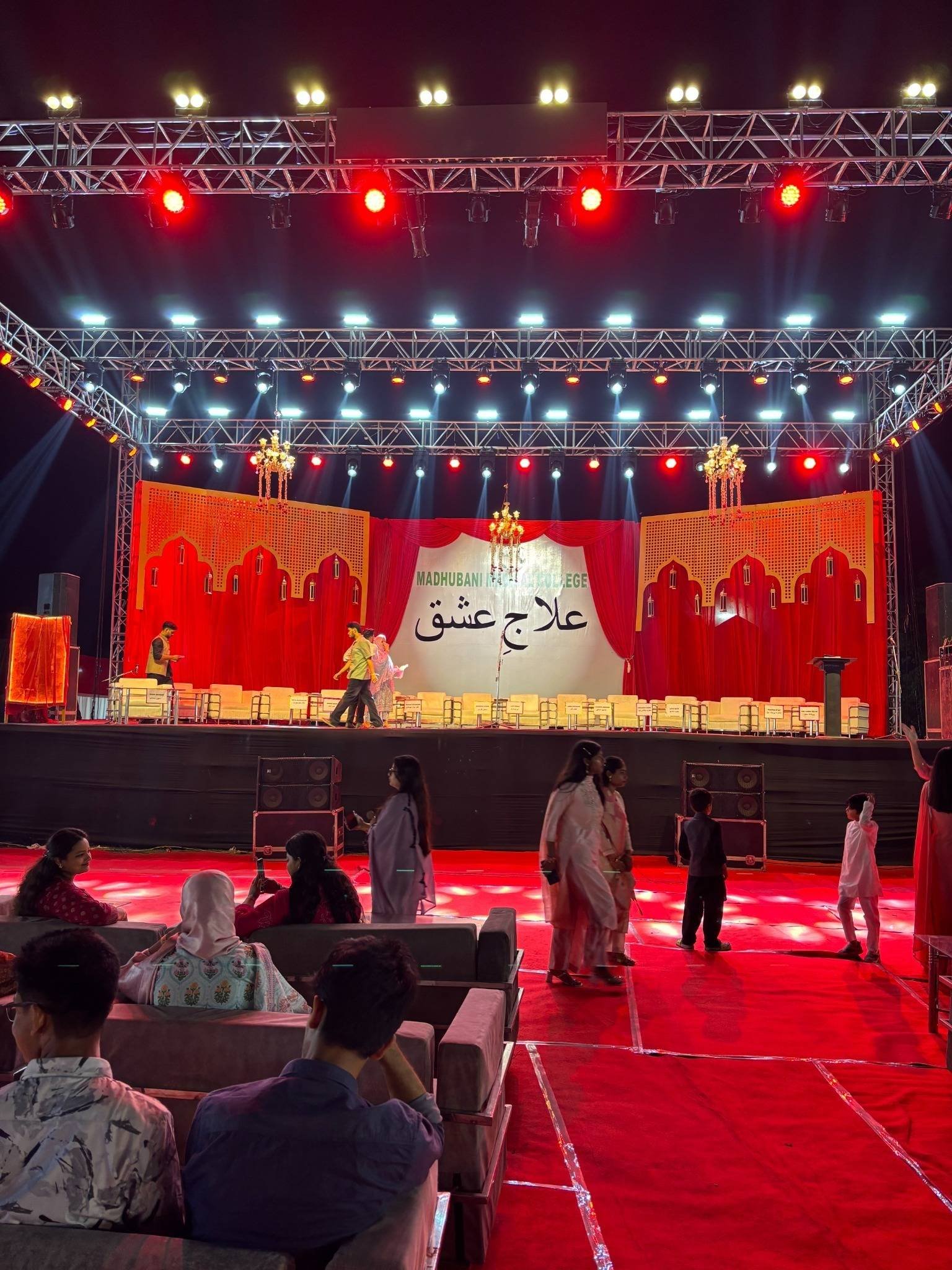 Wide view of the Madhubani Medical College setup: red carpet, seating, chandeliers and arched stage décor under heavy truss lighting.