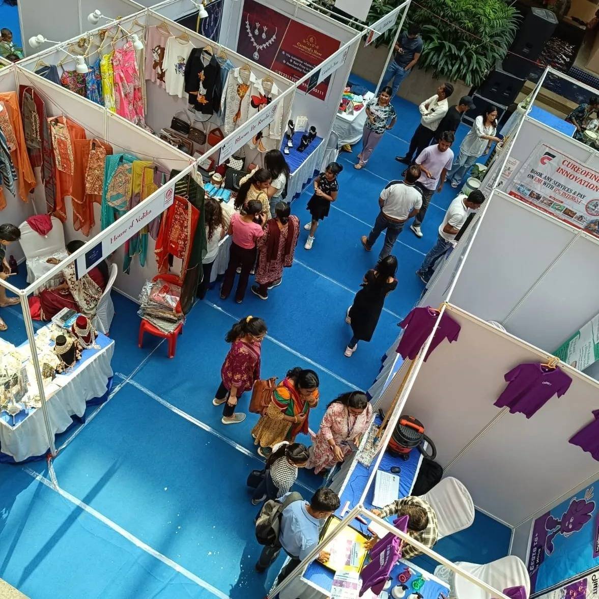 Overhead view of exhibition stalls and visitors on a blue carpet.