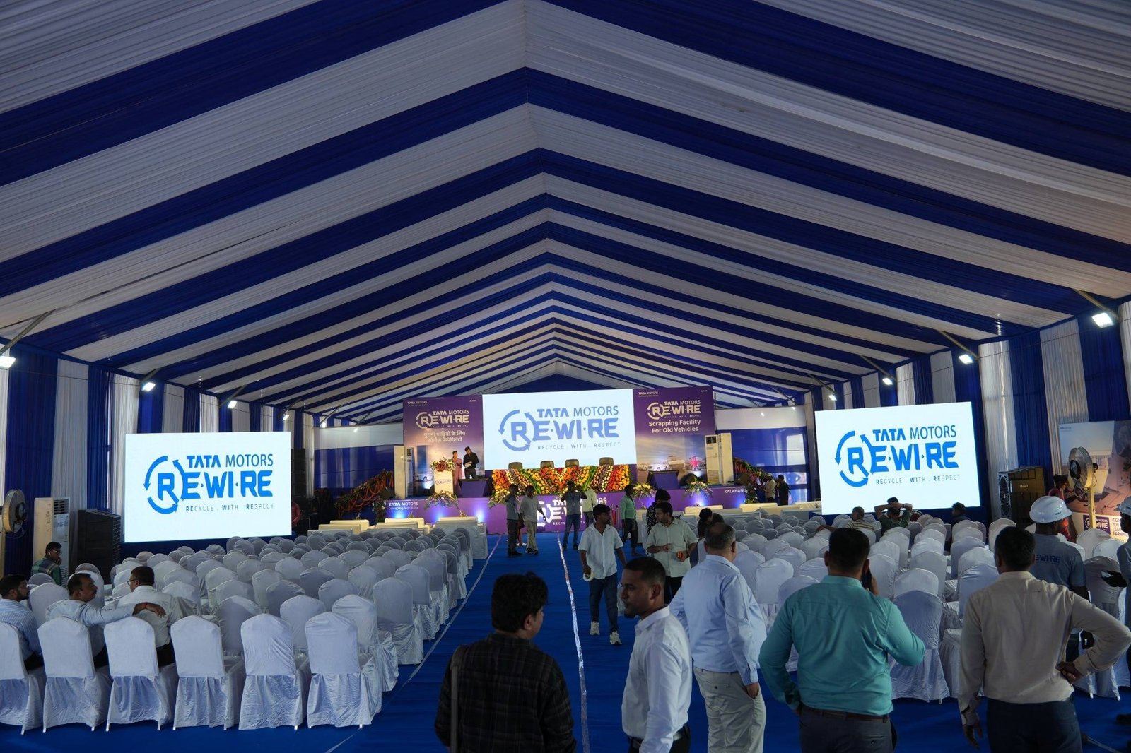 Inside the German hangar for Tata Motors Re.Wi.Re: blue-and-white draped ceiling, rows of covered seating and branded LED screens.
