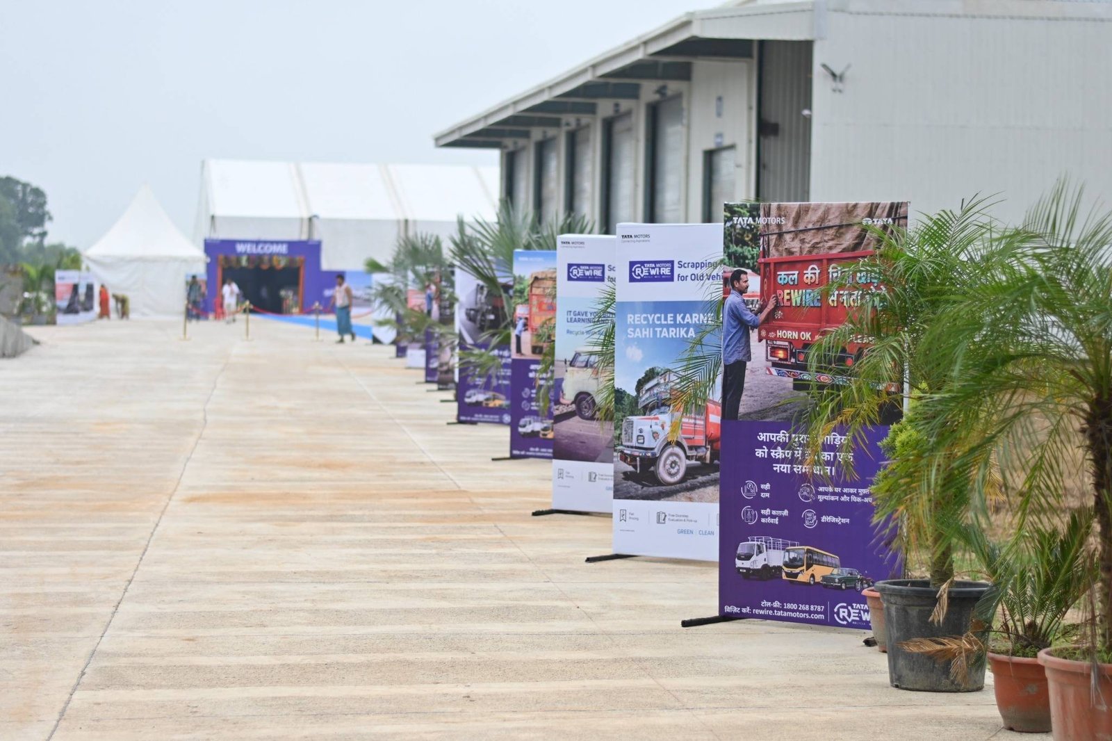 Outdoor route lined with Tata Motors Re.Wi.Re branded standees and plants, leading to the hangar.