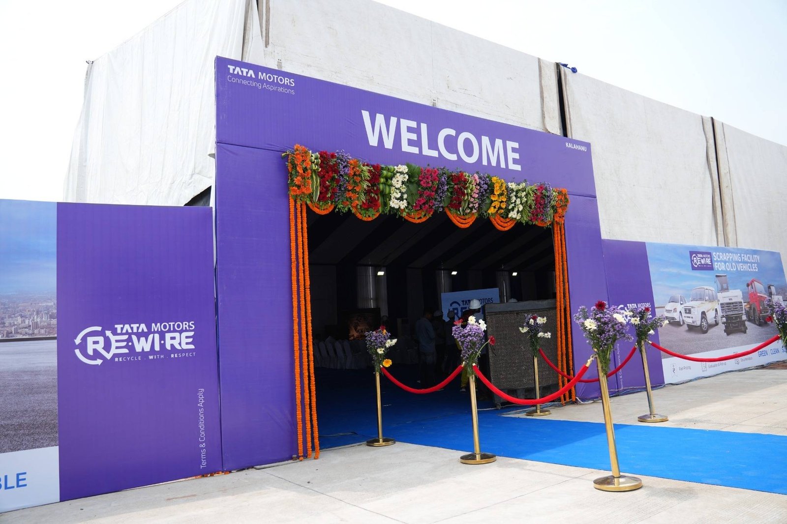 Purple Tata Motors Re.Wi.Re welcome façade with a floral entrance, blue carpet and stanchions.